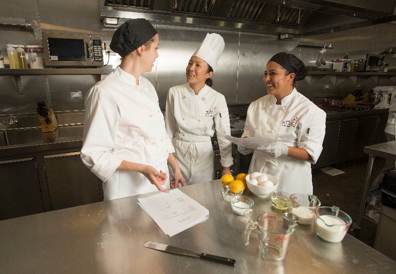 A professor discusses culinary management with students in their kitchen laboratory.